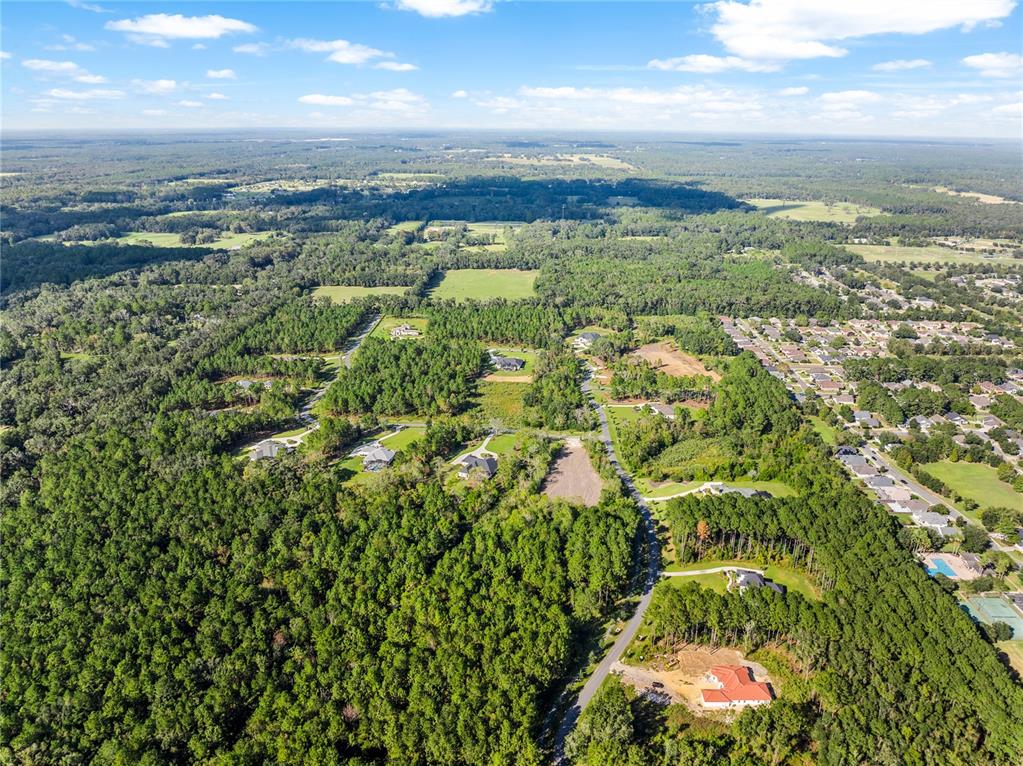 An aerial view shows a residential neighborhood surrounded by dense forest and open fields — TBD NW 150TH BOULEVARD, NEWBERRY, FL