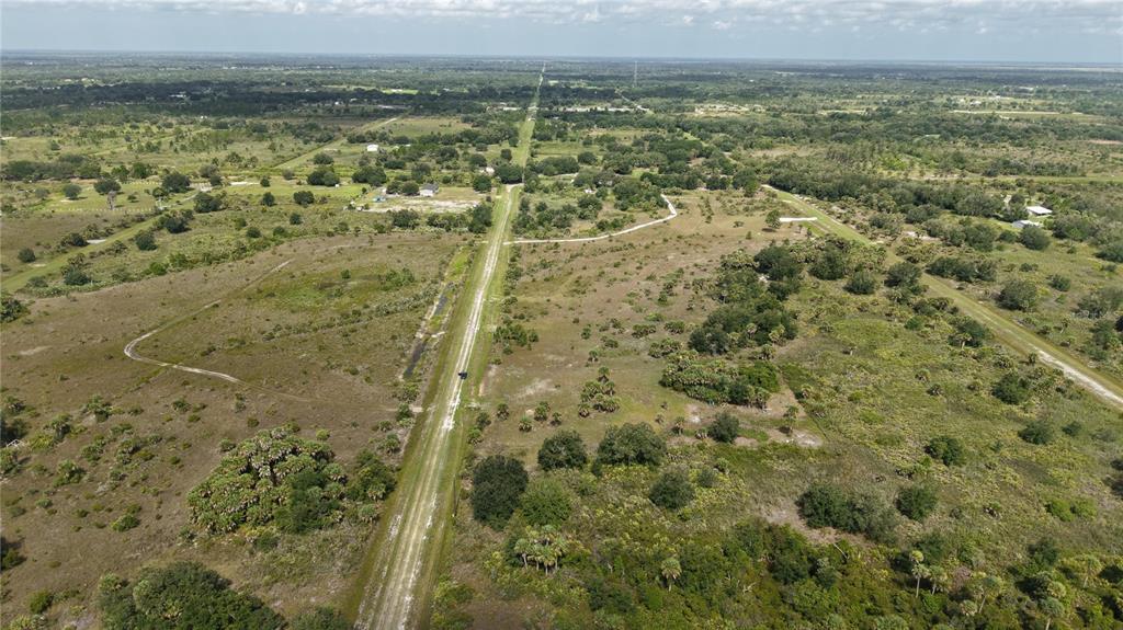 An aerial view shows a dirt road cutting through a large, undeveloped grassy field — 14773 NW 280TH STREET, OKEECHOBEE, FL