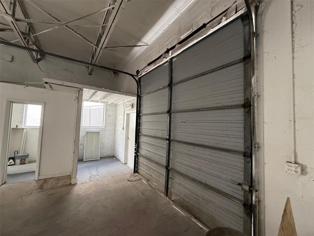 An industrial space featuring a large metal roll-up door, concrete floors, and exposed ceiling trusses — 14020 NW 19TH AVENUE, OPA LOCKA, FL