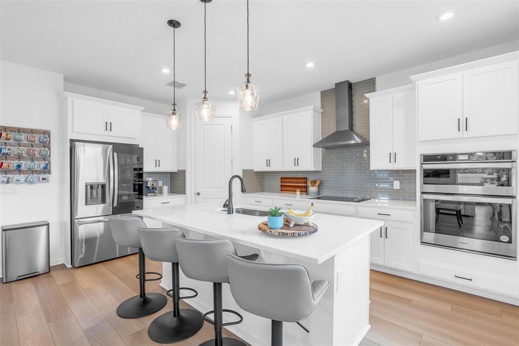 A modern kitchen features white cabinetry, stainless steel appliances, a central island, and gray tile — 2215 BLUE SALVIA STREET, CLERMONT, FL