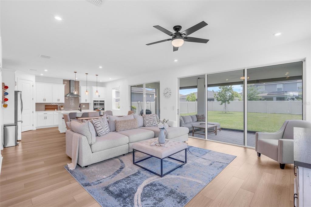 An open-concept living room features a light gray sectional, patterned rug, and sliding glass doors — 2215 BLUE SALVIA STREET, CLERMONT, FL