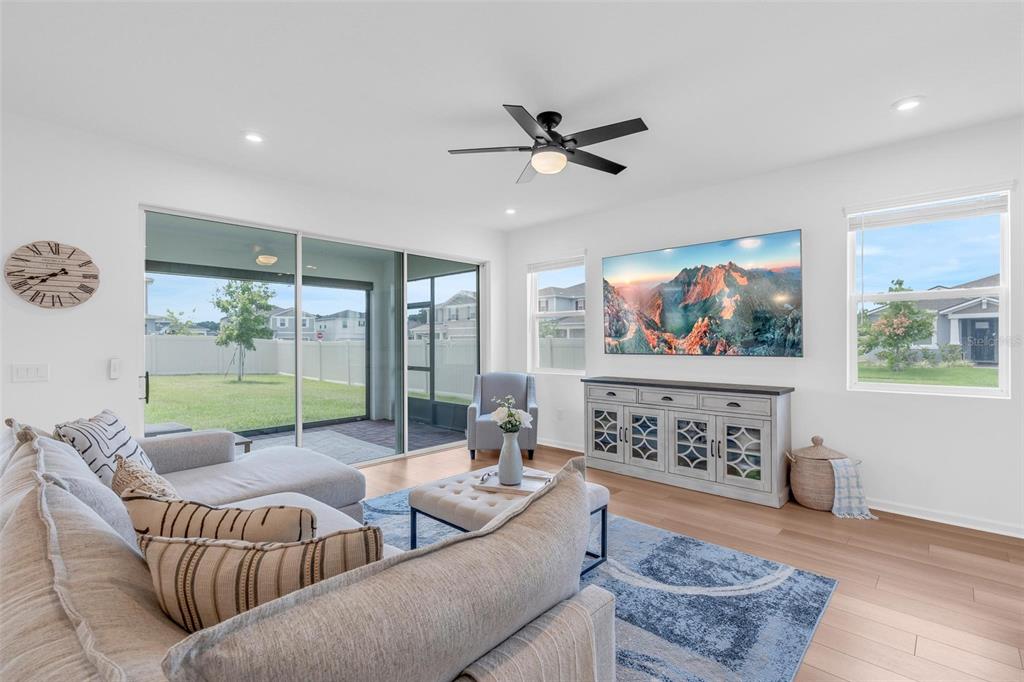 A living room features a sectional sofa, a television, a media console, and sliding glass doors — 2215 BLUE SALVIA STREET, CLERMONT, FL