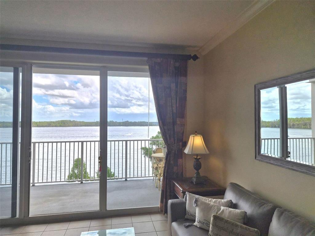 A living room with a sliding glass door leading to a balcony overlooking a lake — 13427 BLUE HERON BEACH DRIVE UNIT 402, ORLANDO, FL
