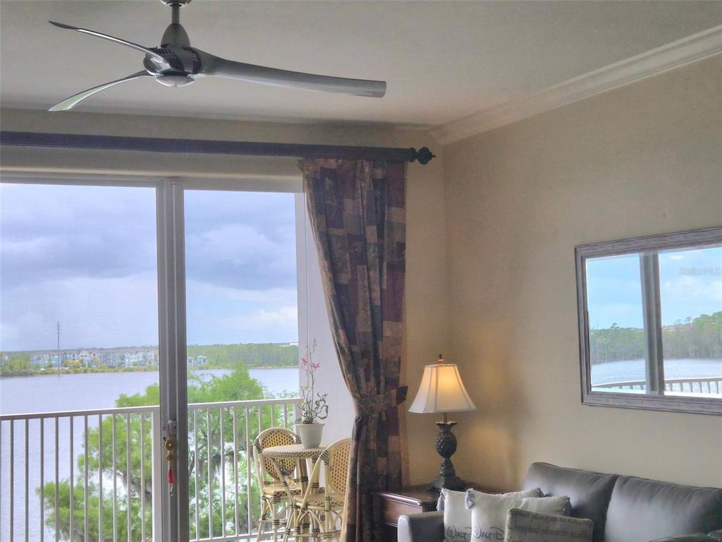 A living room features a ceiling fan, a leather sofa, and a balcony overlooking water — 13427 BLUE HERON BEACH DRIVE UNIT 402, ORLANDO, FL