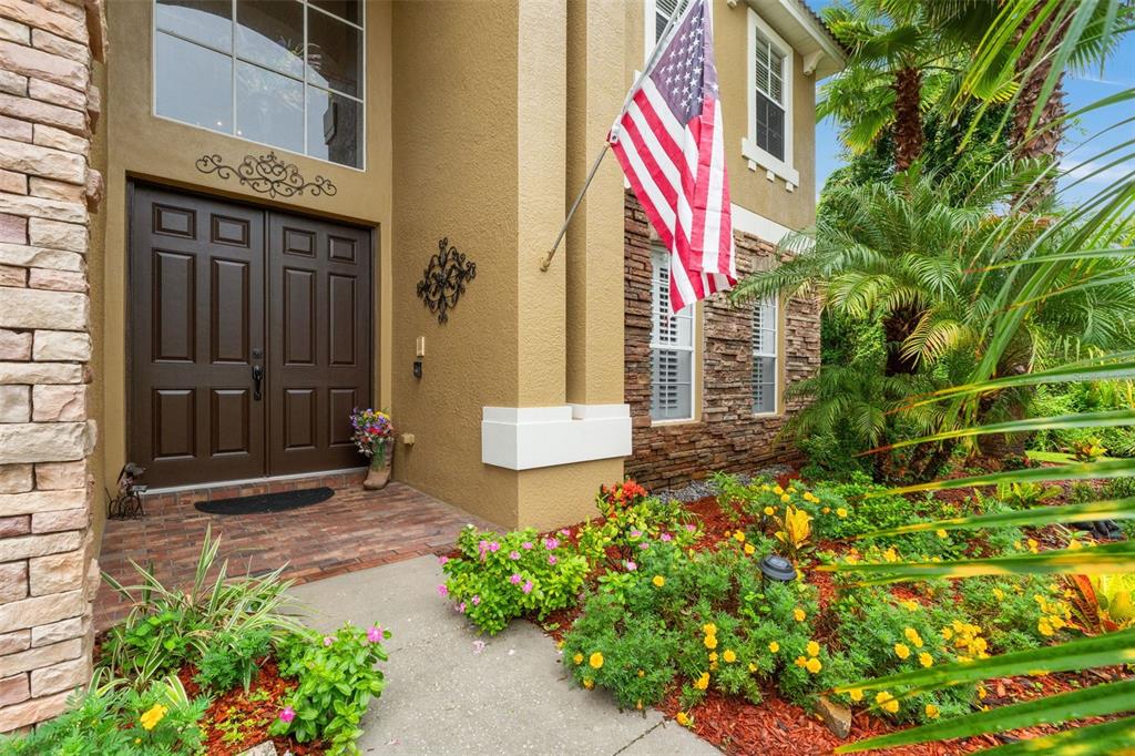 A brown double front door with an American flag and landscaping in the front yard — 7445 MINNOW BROOK WAY, LAND O LAKES, FL
