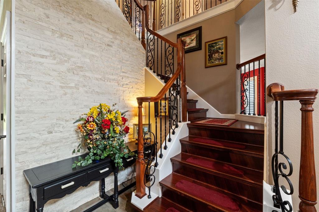A staircase with dark wood steps and iron railings sits beside a stone accent wall — 7445 MINNOW BROOK WAY, LAND O LAKES, FL