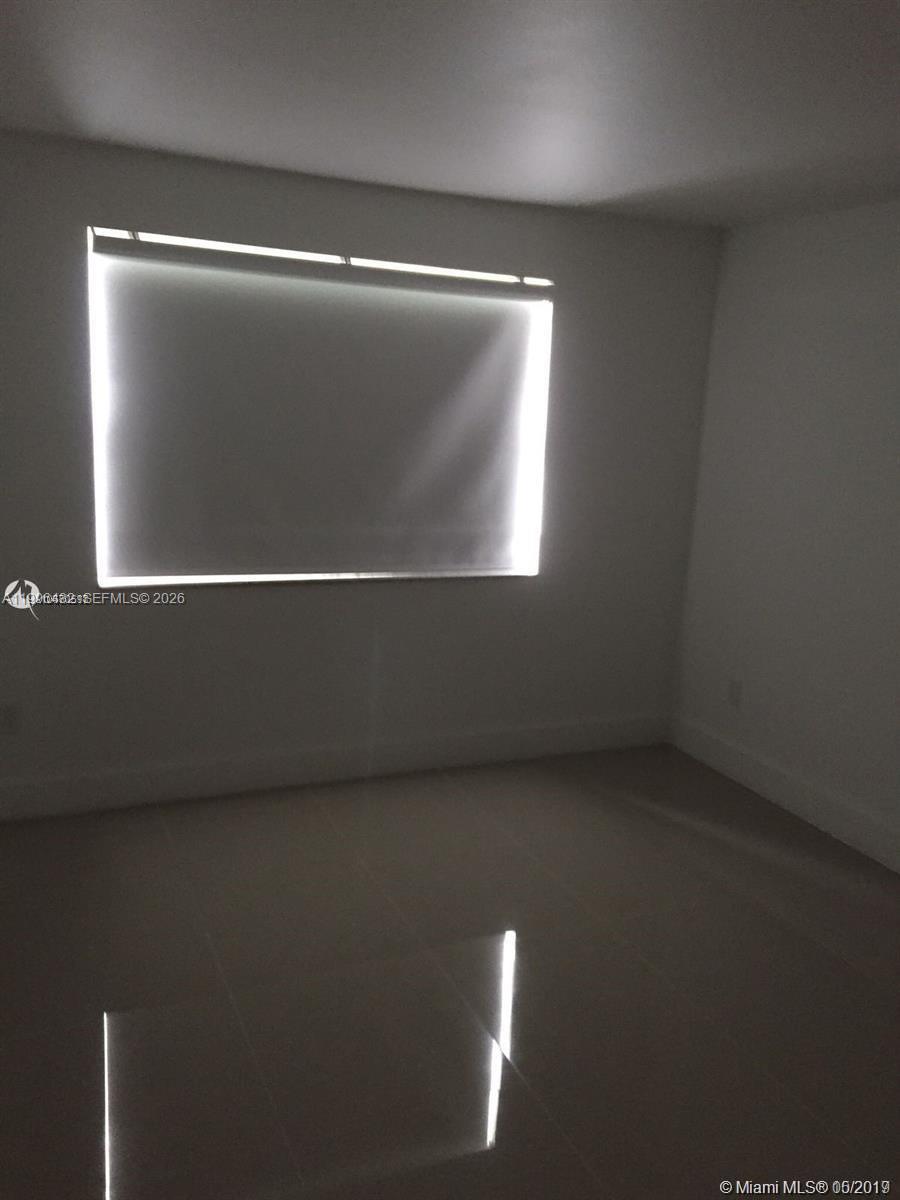 A sparsely furnished room features white walls, light-colored tile flooring, and a bright window — 4600 NW 79th Ave # 1B, Doral FL 33166, DORAL, FL