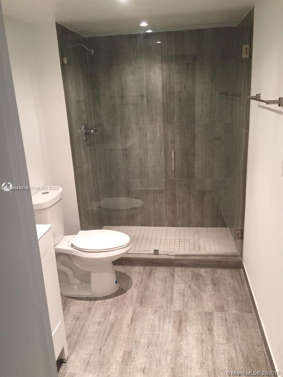 A bathroom features a glass-enclosed walk-in shower with gray wood-look tile and matching flooring — 4600 NW 79th Ave # 1B, Doral FL 33166, DORAL, FL