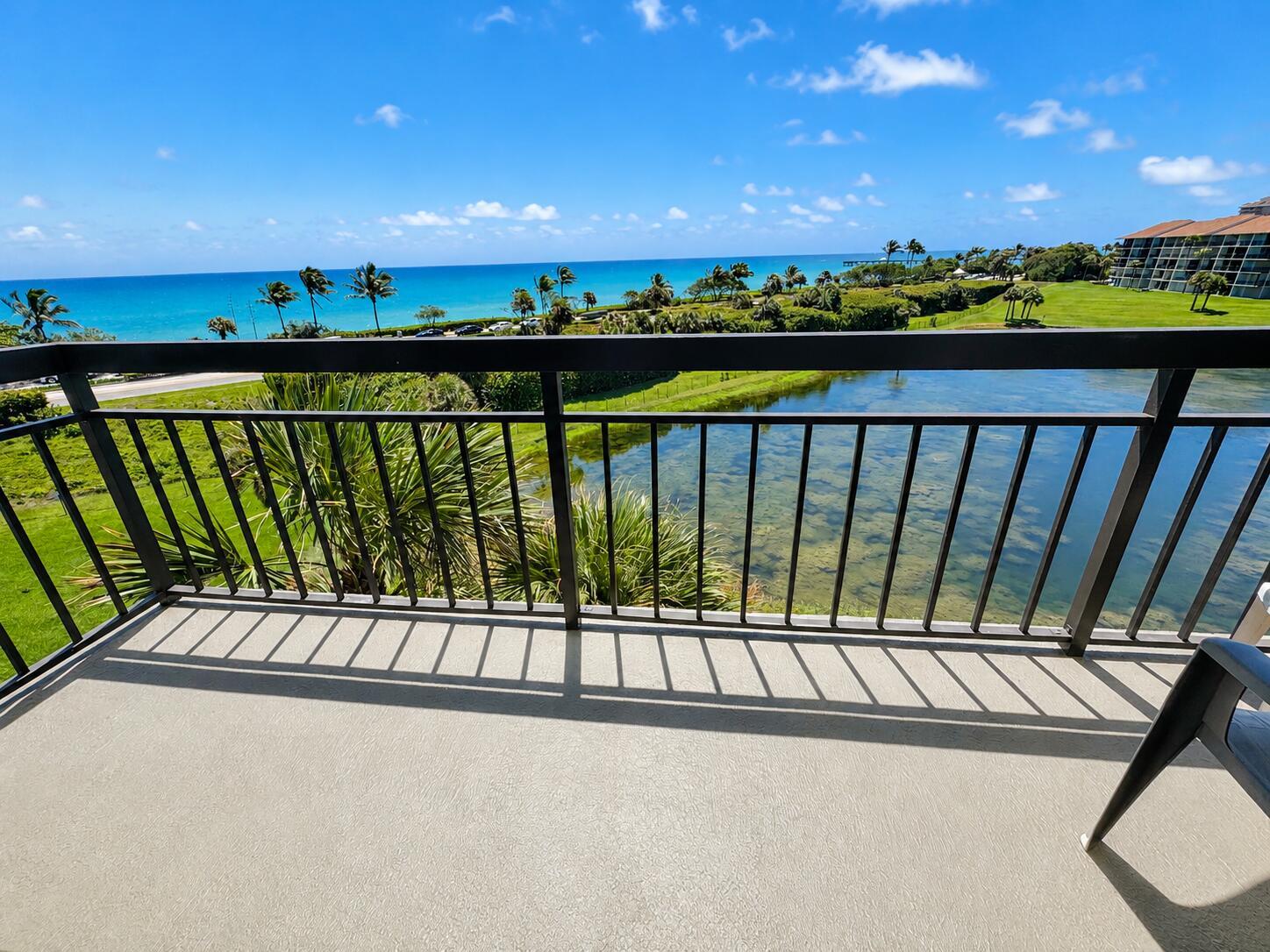 A balcony with a metal railing overlooks a pond, lush landscaping, and the ocean — 101 S Seas Drive # 505, Jupiter FL 33477, JUPITER, FL