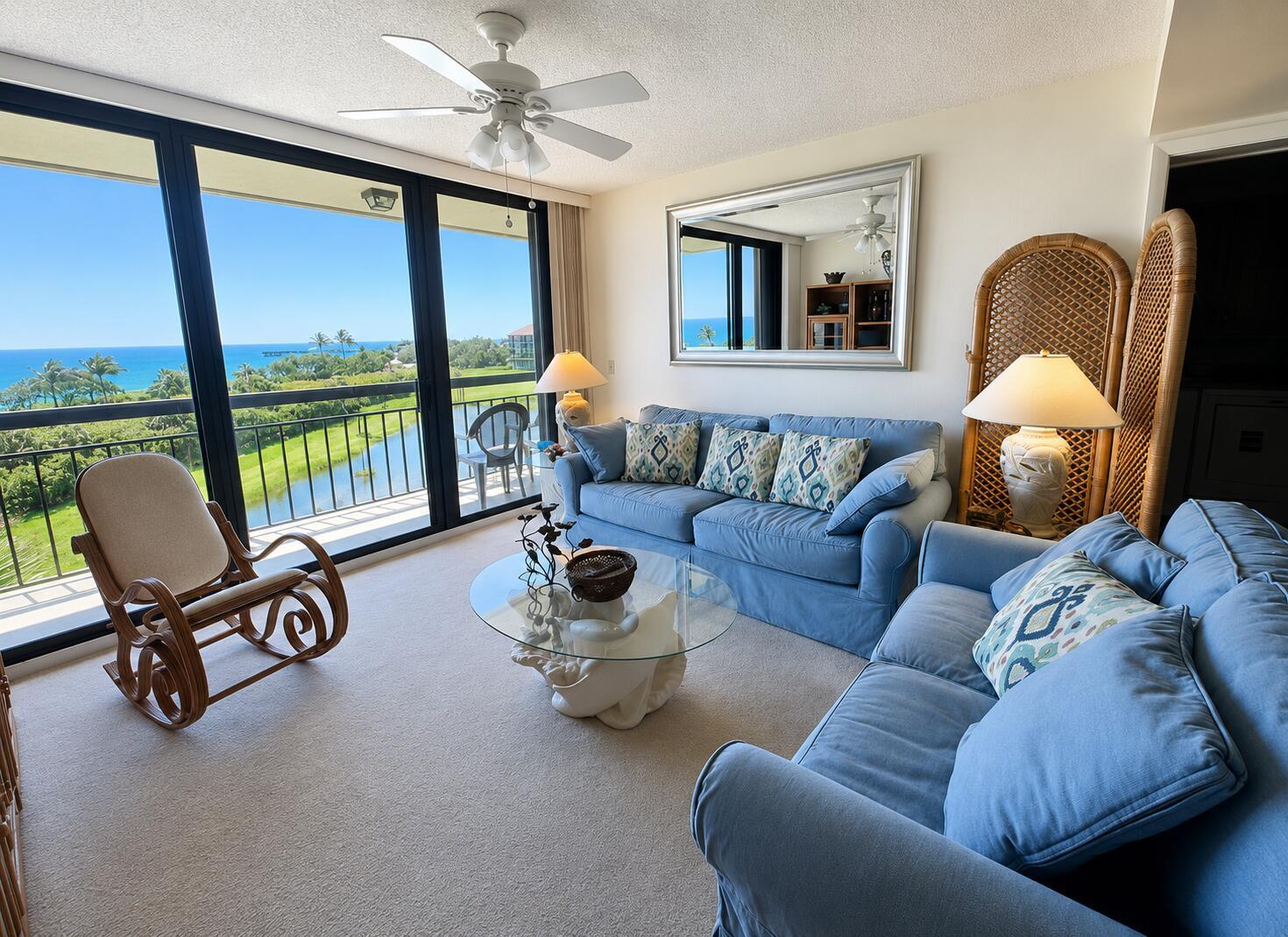A living room with blue sofas, a glass coffee table, and a balcony overlooking the ocean — 101 S Seas Drive # 505, Jupiter FL 33477, JUPITER, FL