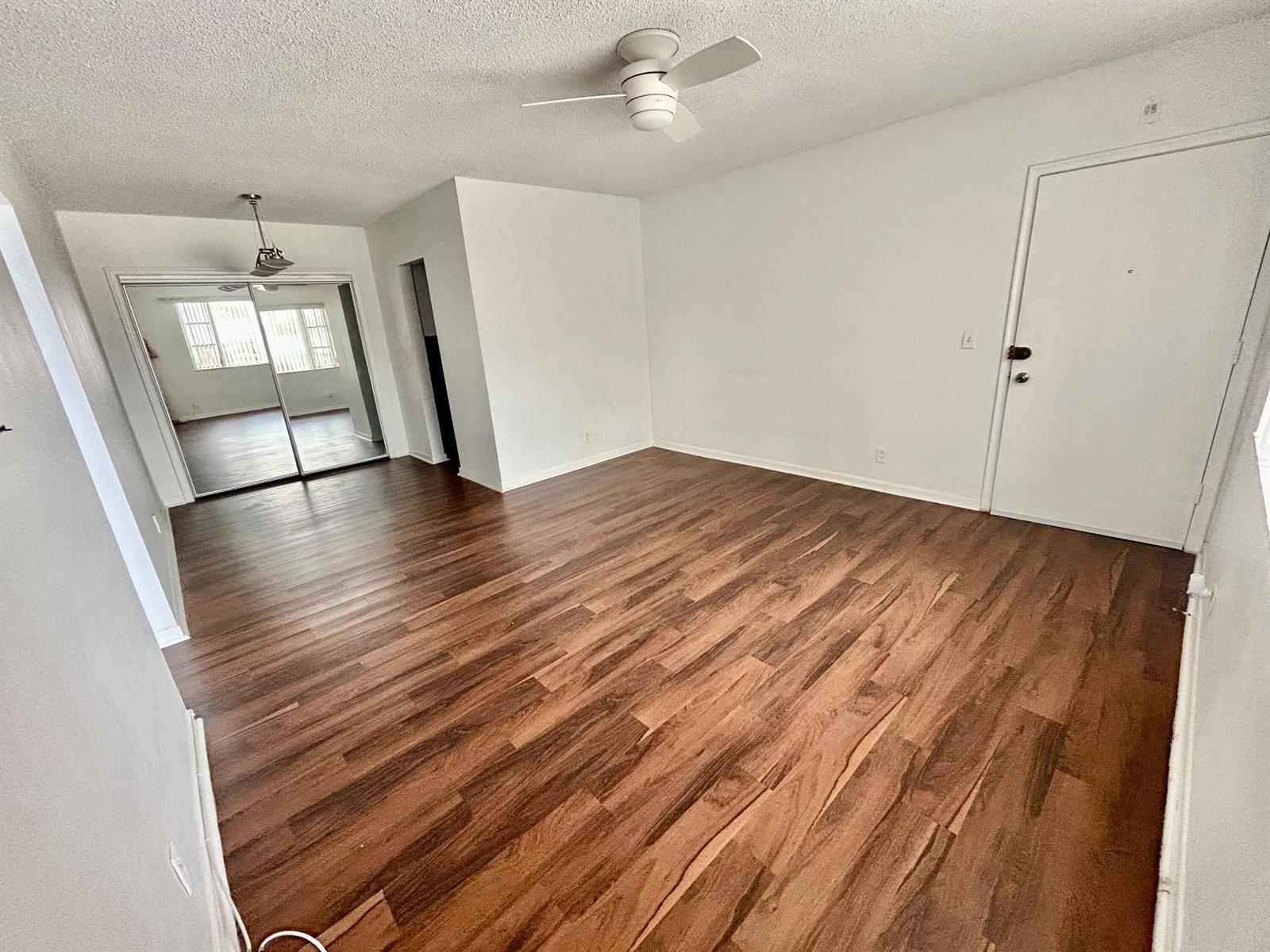 An empty room features wood-look flooring, white walls, a ceiling fan, and mirrored closet doors — 350 S Cypress Road # 521, Pompano Beach FL 33060, POMPANO BEACH, FL