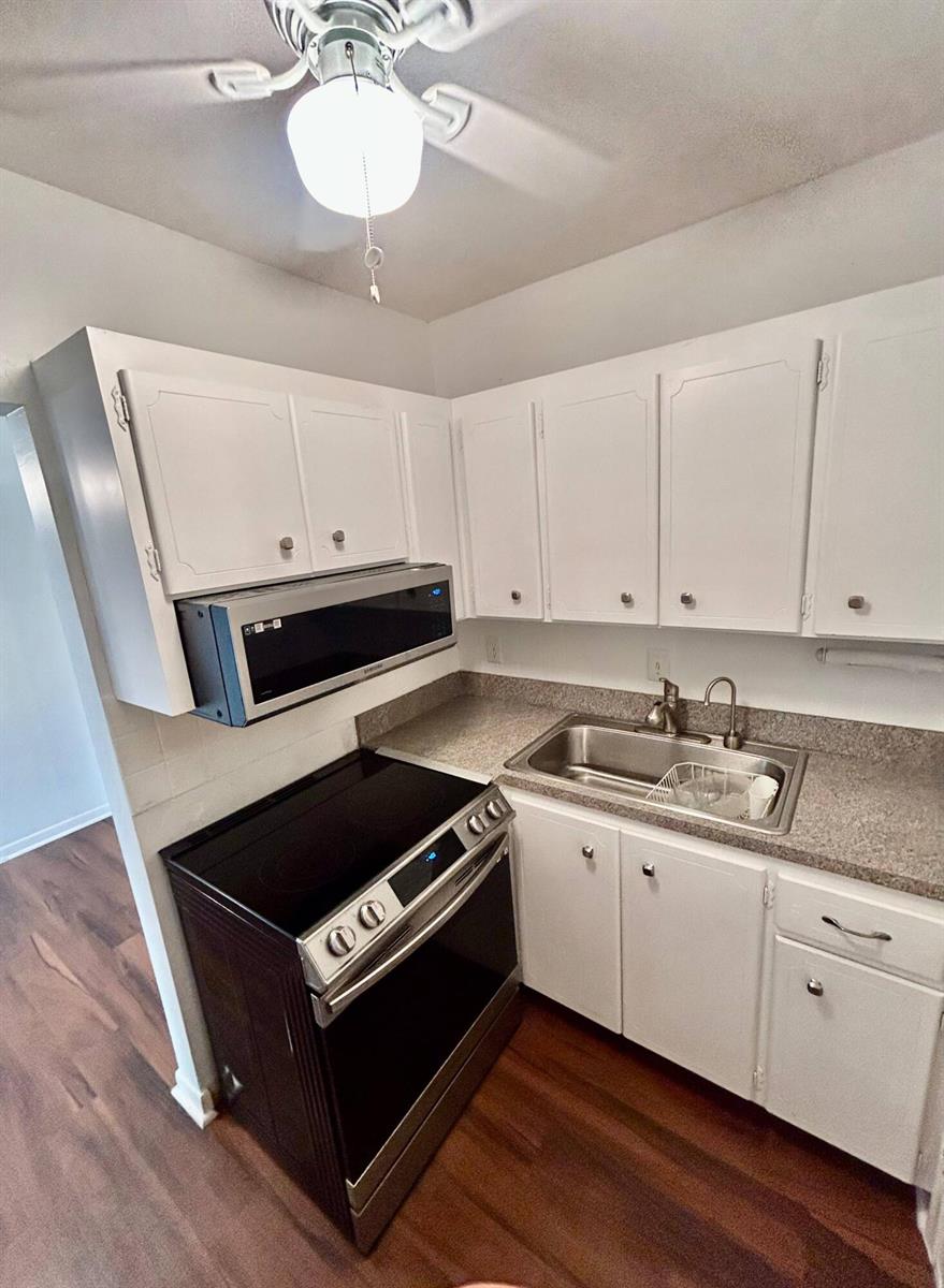 A kitchen features white cabinets, a black electric stove, a microwave, and a stainless sink — 350 S Cypress Road # 521, Pompano Beach FL 33060, POMPANO BEACH, FL