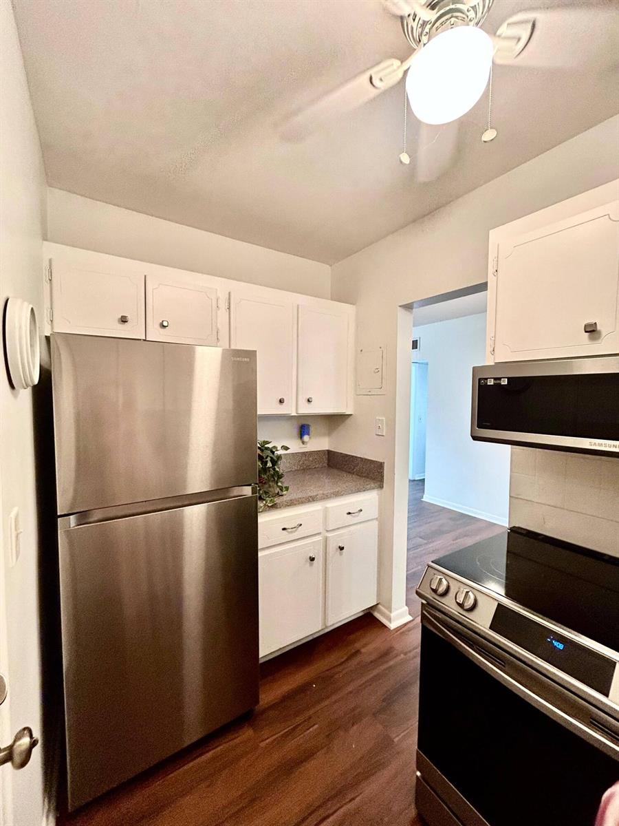 A kitchen features white cabinets, stainless steel appliances, a granite countertop, and wood-look flooring — 350 S Cypress Road # 521, Pompano Beach FL 33060, POMPANO BEACH, FL