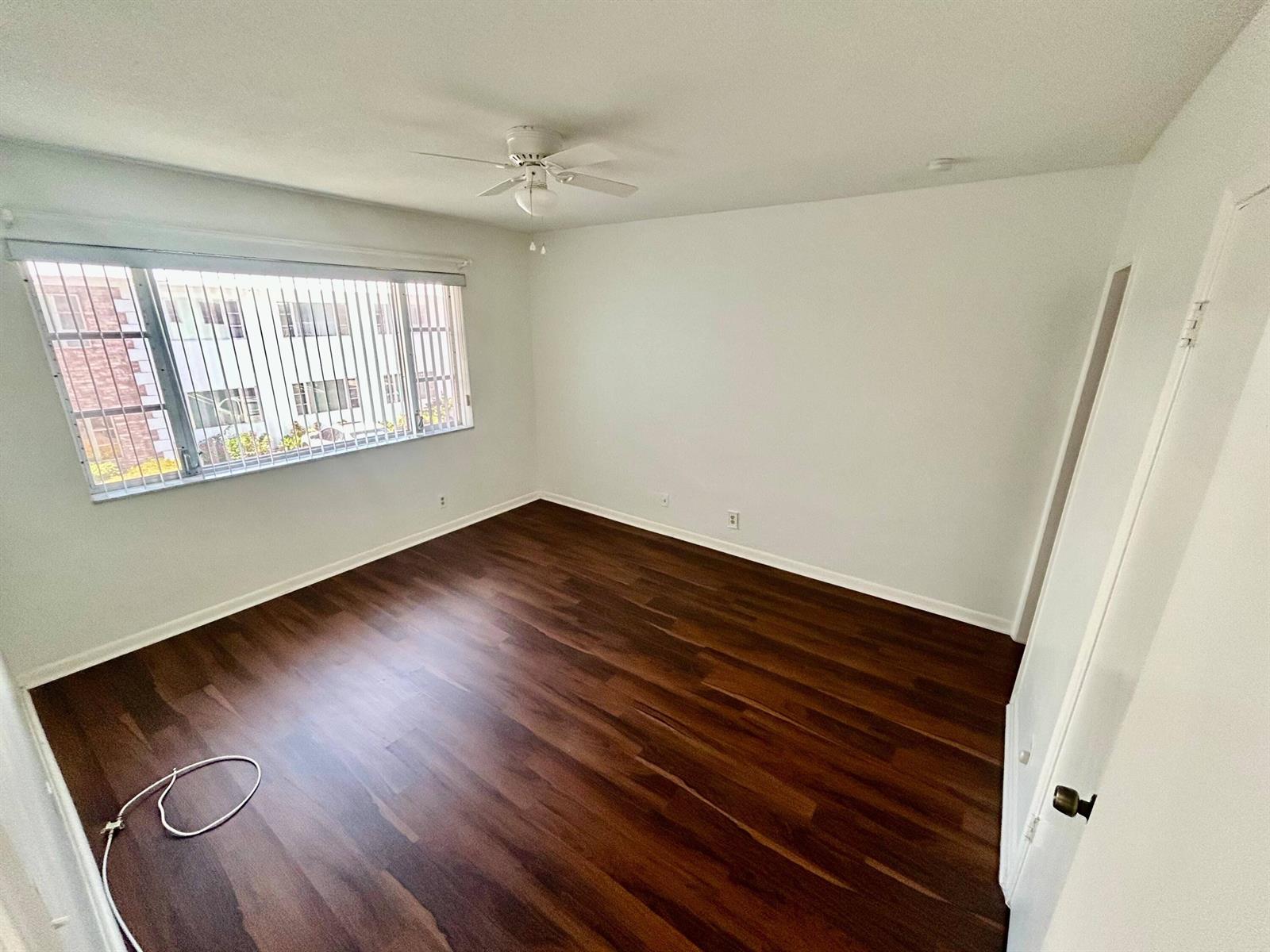 An empty bedroom features dark wood flooring, white walls, a ceiling fan, and vertical blinds — 350 S Cypress Road # 521, Pompano Beach FL 33060, POMPANO BEACH, FL
