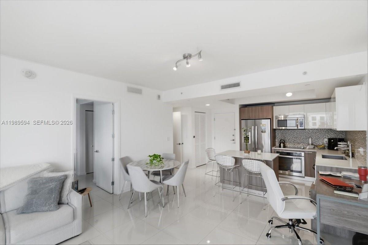 This open-concept living area features a dining space, kitchen island, and modern white cabinetry — 5300 Paseo Blvd # 1803, Doral FL 33166, DORAL, FL
