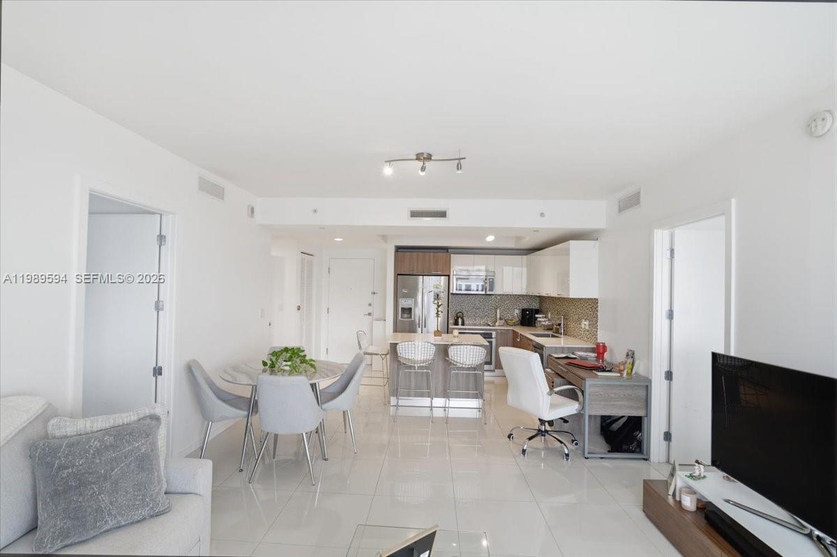 An open-concept living area features a kitchen with white cabinets, a dining table, and tile flooring — 5300 Paseo Blvd # 1803, Doral FL 33166, DORAL, FL