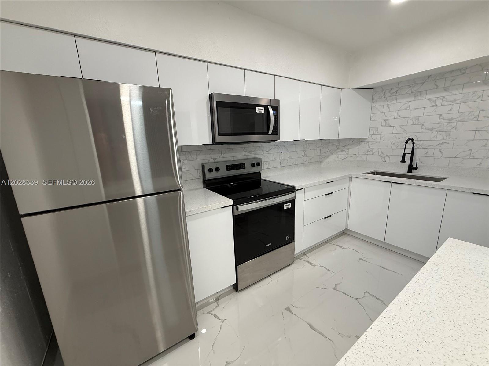 A modern kitchen features white cabinets, stainless steel appliances, and marble-patterned tile flooring and backsplash — 6520 W 8th Ln # 2, Hialeah FL 33012, HIALEAH, FL