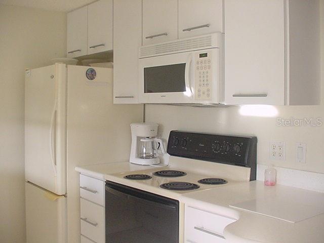A kitchen features white cabinetry, a white refrigerator, a microwave, and a black electric stove — 519 CIRCLEWOOD DRIVE UNIT 519, VENICE, FL