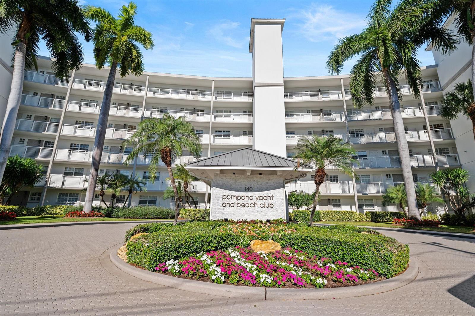 The exterior of a multi-story apartment building features a circular driveway and landscaped garden — 140 NE 28th Avenue # 406, Pompano Beach FL 33062, POMPANO BEACH, FL