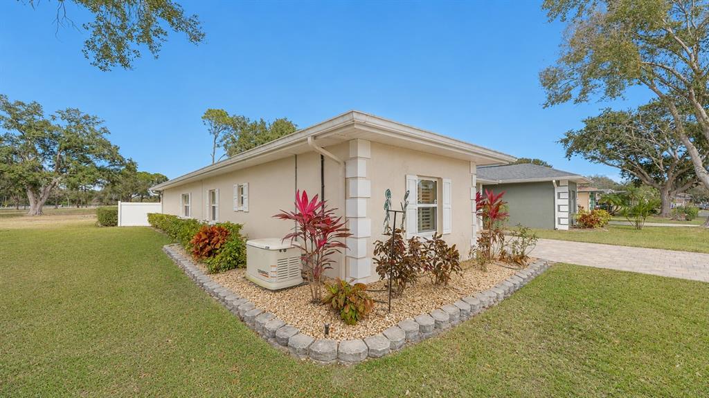The side exterior of a beige house features a Generac generator and landscaped garden beds — 728 CANBERRA ROAD, WINTER HAVEN, FL