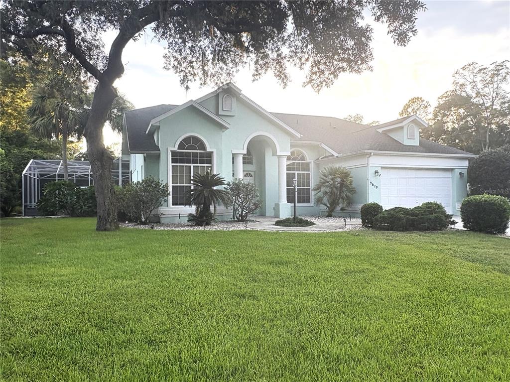 A light green single-story house features a white garage, arched windows, and a screened lanai — 9670 SW 190TH TERRACE ROAD, DUNNELLON, FL