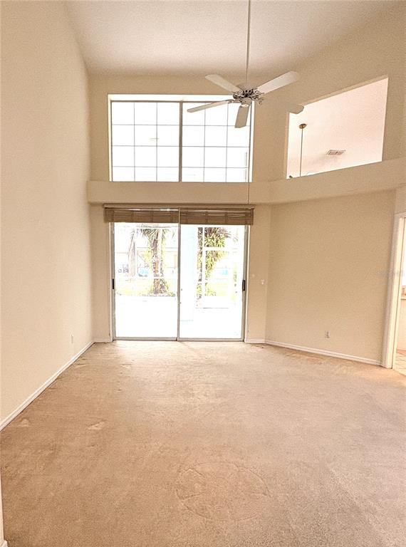 A living room features high ceilings, beige carpeting, a ceiling fan, and large windows — 9670 SW 190TH TERRACE ROAD, DUNNELLON, FL