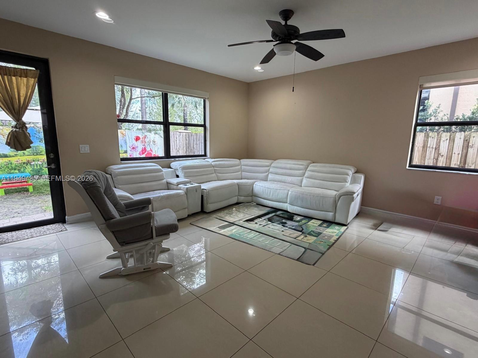 A living room features a white sectional sofa, a grey rocking chair, and tile flooring — 9855 NW 89th Ter, Doral FL 33178, DORAL, FL
