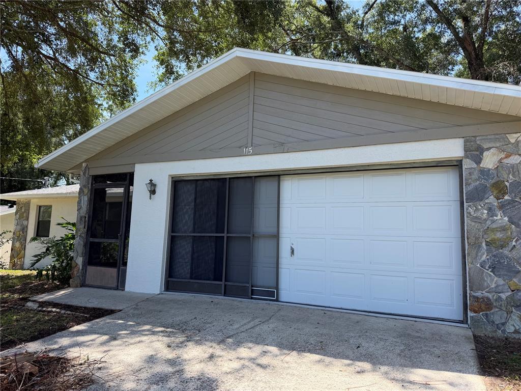 A single-story house exterior features a garage, a screened-in entryway, and stone facade accents — 115 DAFFODILL STREET, INVERNESS, FL