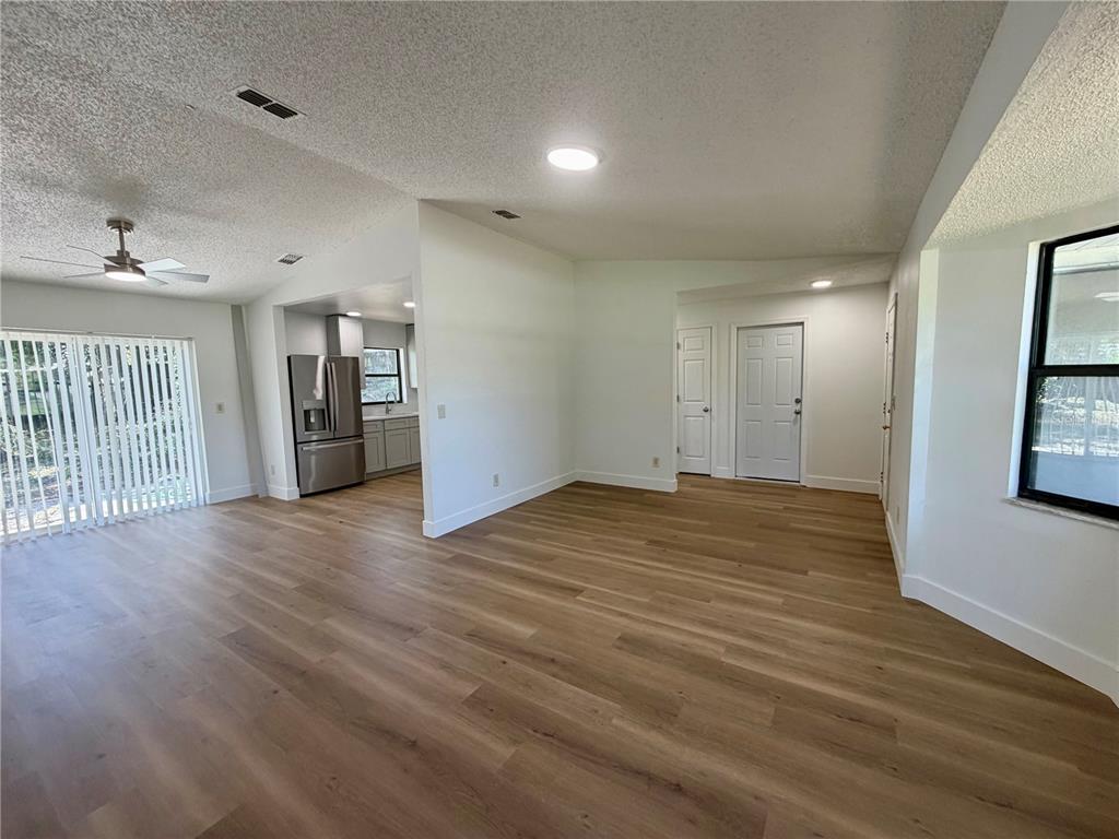 An open-concept living area features light wood-look flooring, white walls, and an adjacent kitchen — 115 DAFFODILL STREET, INVERNESS, FL