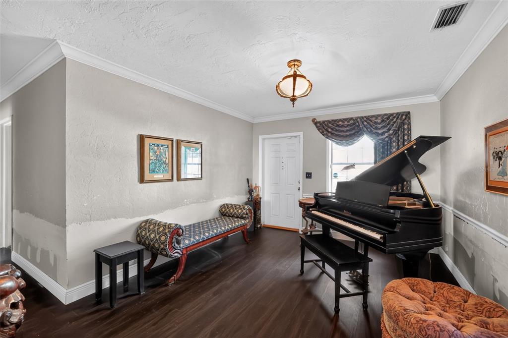 A room with dark wood flooring, a grand piano, a patterned bench, and a light fixture — 4204 S RENELLIE DRIVE, TAMPA, FL