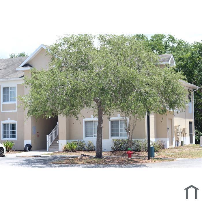 A two-story apartment building with beige stucco siding and a large tree in front — 6022 PORTSDALE PLACE UNIT 202, RIVERVIEW, FL
