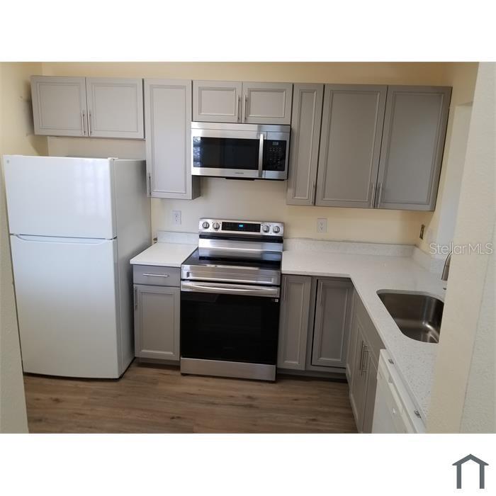 A kitchen features gray cabinets, stainless steel appliances, white countertops, and wood-look flooring — 6022 PORTSDALE PLACE UNIT 202, RIVERVIEW, FL