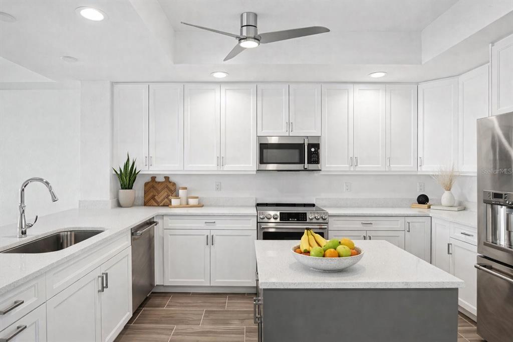 A modern kitchen features white cabinets, quartz countertops, stainless steel appliances, and a gray island — 125 ISLAND WAY UNIT 304, CLEARWATER BEACH, FL