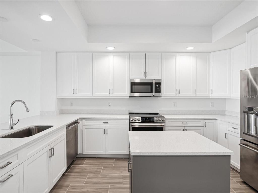A modern kitchen features white cabinets, stainless steel appliances, quartz countertops, and a gray island — 125 ISLAND WAY UNIT 304, CLEARWATER BEACH, FL