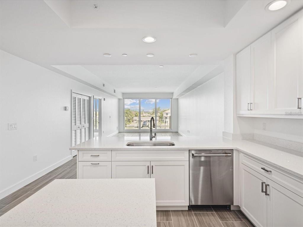 A bright kitchen features white cabinets, quartz countertops, a stainless dishwasher, and wood-look tile flooring — 125 ISLAND WAY UNIT 304, CLEARWATER BEACH, FL
