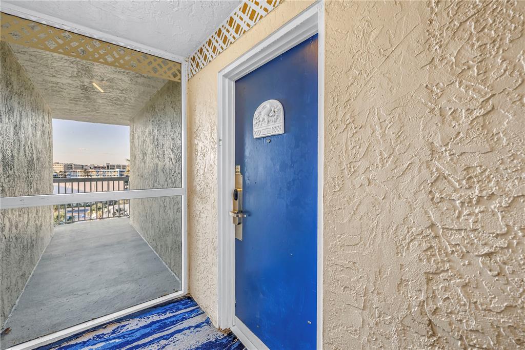 A blue door with a decorative plaque sits on a balcony with textured walls — 5500 GULF BOULEVARD UNIT 6248, ST PETE BEACH, FL