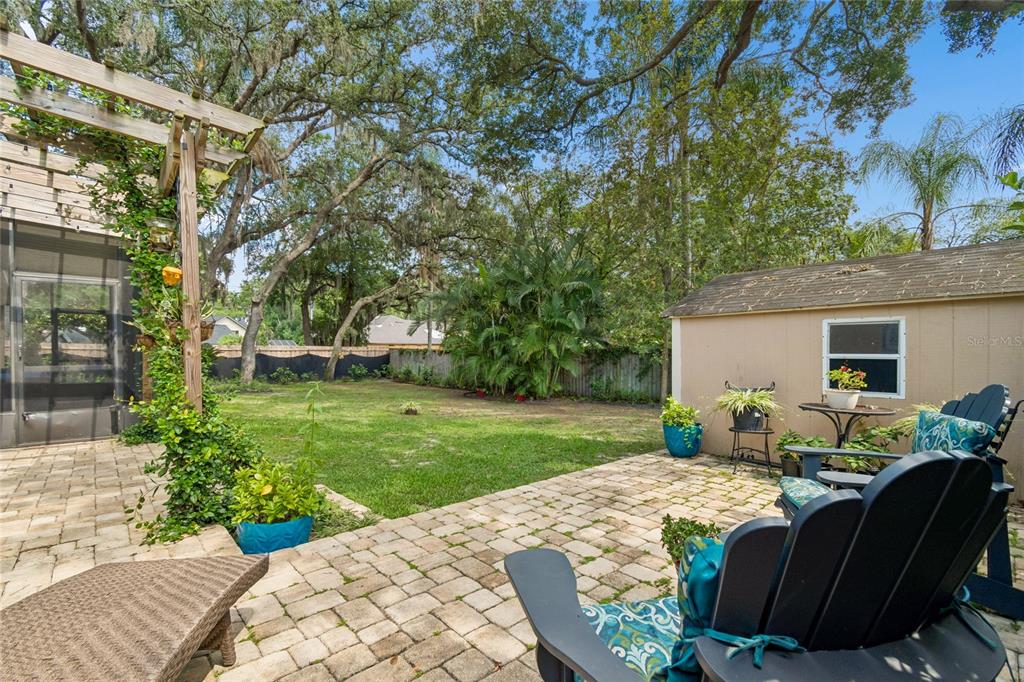 A backyard features a stone patio, a wooden shed, and a grassy lawn under trees — 3602 ARLINGTON OAKS COURT, TAMPA, FL