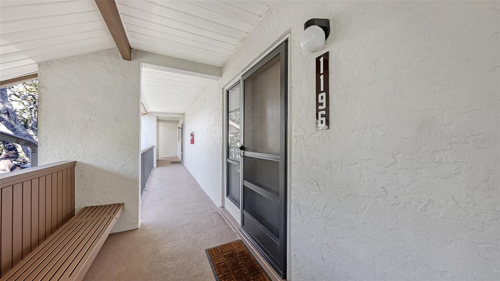 An exterior view of a covered apartment walkway featuring a bench and a screen door — 1196 BIRD BAY WAY UNIT 310, VENICE, FL
