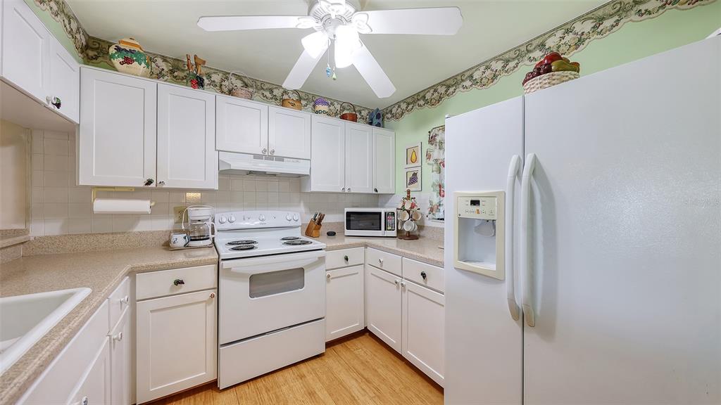 A kitchen features white cabinets, white appliances, light countertops, and a ceiling fan — 1196 BIRD BAY WAY UNIT 310, VENICE, FL