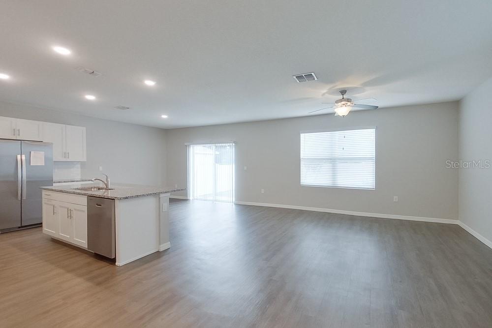 An open-concept kitchen and living area features white cabinets, a granite island, and wood-look flooring — 31978 KATELIN CIRCLE, LEESBURG, FL
