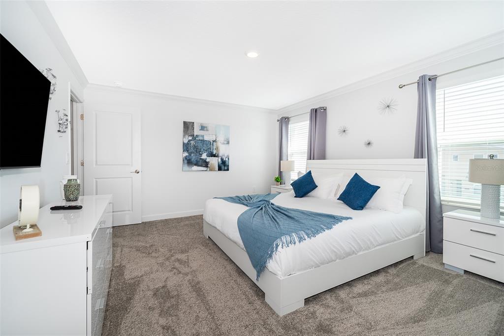 A bedroom features a white bed with blue accents, gray carpeting, and white walls — 1164 KINGSBARN STREET, DAVENPORT, FL