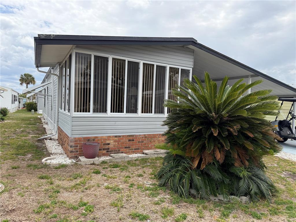 The exterior of a manufactured home features a brick base, gray siding, and a sunroom — 4038 ROLLING OAKS DRIVE, WINTER HAVEN, FL