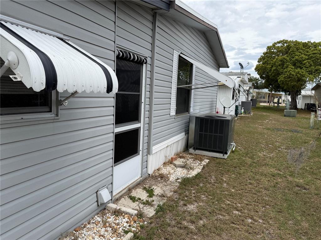 The exterior of a gray mobile home features a screen door, window awnings, and an AC unit — 4038 ROLLING OAKS DRIVE, WINTER HAVEN, FL