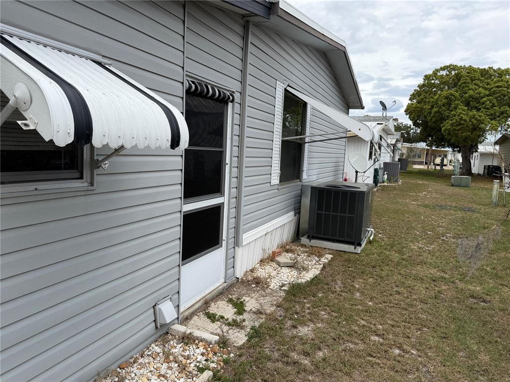 The exterior side of a gray-sided mobile home features a door, awning, and AC unit — 4038 ROLLING OAKS DRIVE, WINTER HAVEN, FL