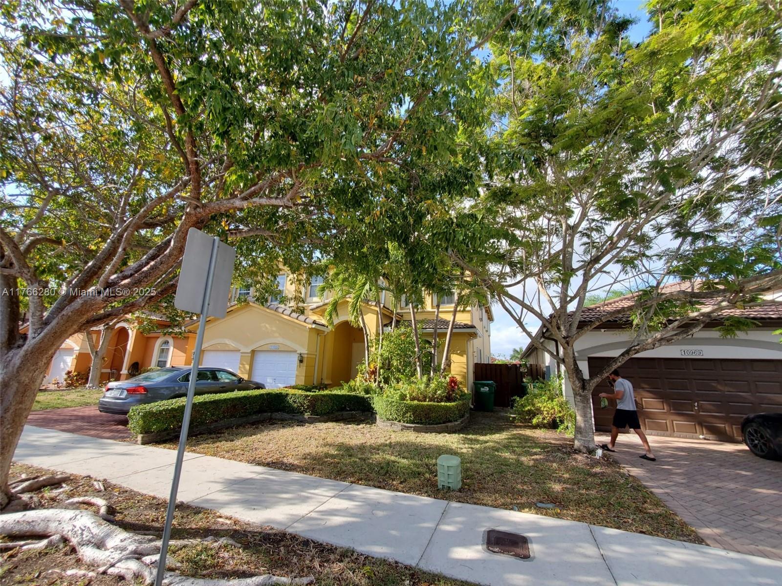 A two-story yellow house with a two-car garage and mature trees in the front yard — 11009 NW 80th Ln, Doral FL 33178, DORAL, FL