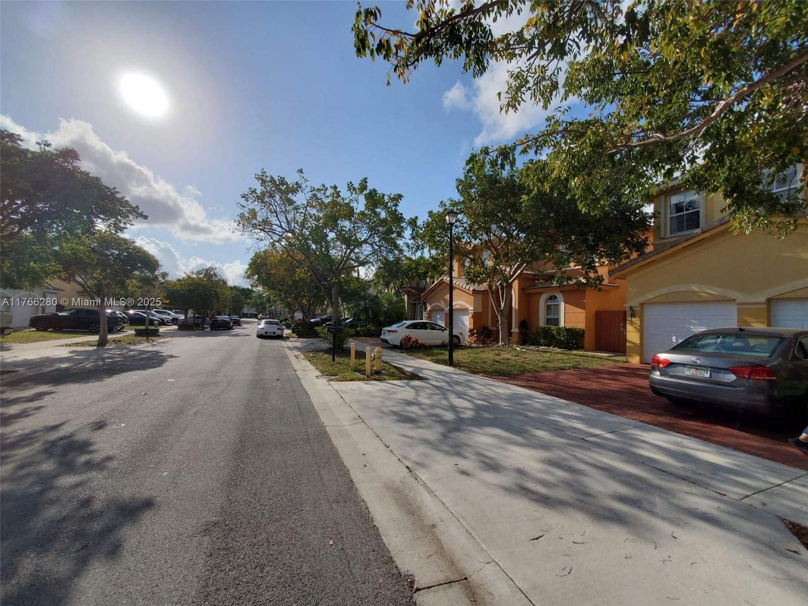 A street view shows residential houses with driveways, parked cars, and trees under a sunny sky — 11009 NW 80th Ln, Doral FL 33178, DORAL, FL