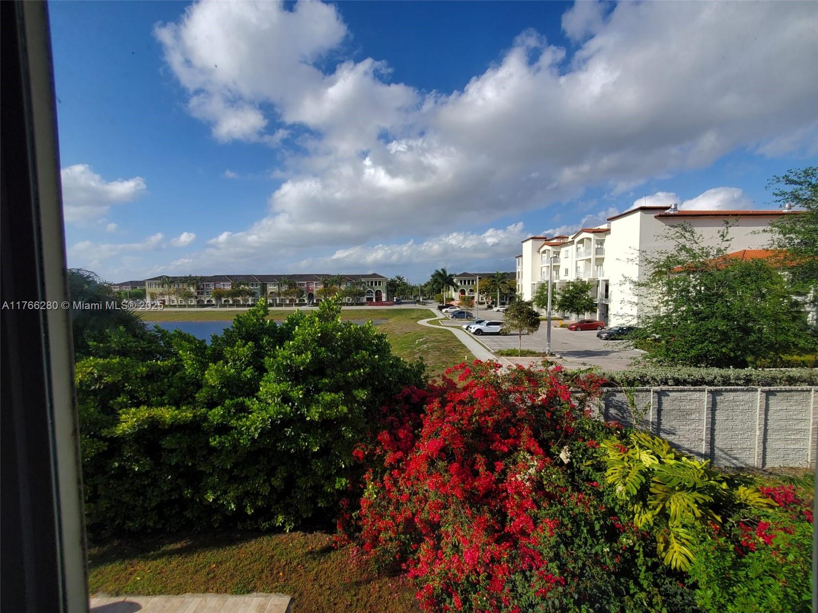 An elevated view shows a lake, apartment buildings, parking lots, and vibrant flowering bushes — 11009 NW 80th Ln, Doral FL 33178, DORAL, FL