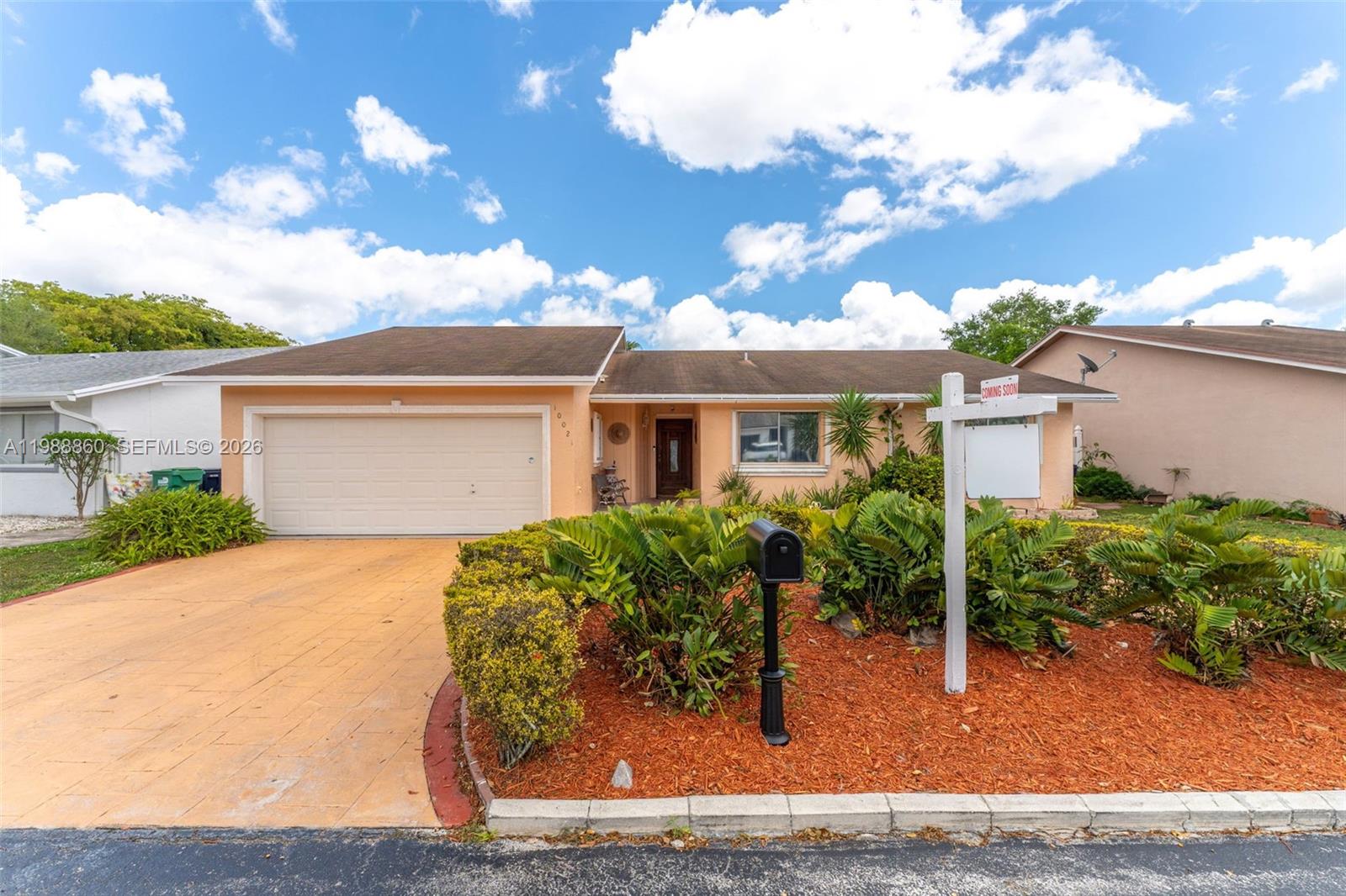 A single-story peach-colored house features a two-car garage, a front yard with landscaping, and a sign — 10021 SW 145th Pl, Miami FL 33186, MIAMI, FL