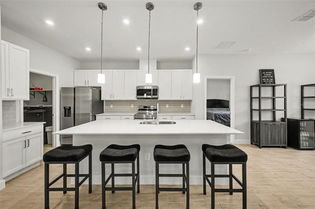 A modern kitchen features white cabinetry, a large central island with bar stools, and stainless appliances — 12 LANSING LANE, PALM COAST, FL