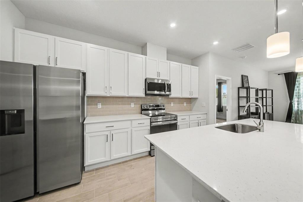 A modern kitchen features white cabinets, stainless steel appliances, and a large quartz island — 12 LANSING LANE, PALM COAST, FL